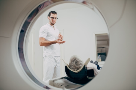 young medical technician talking to patient lying on CT scanner bed